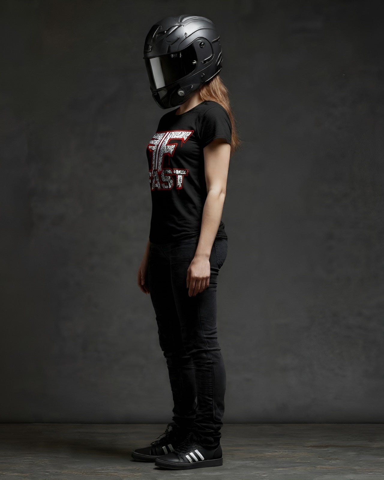 Woman in black jeans, adidas, and a superbike t-shirt, wearing a black motorcycle helmet. This motorcycle enthusiast apparel art shirt features a red and white graphic inspired by Alec M.
