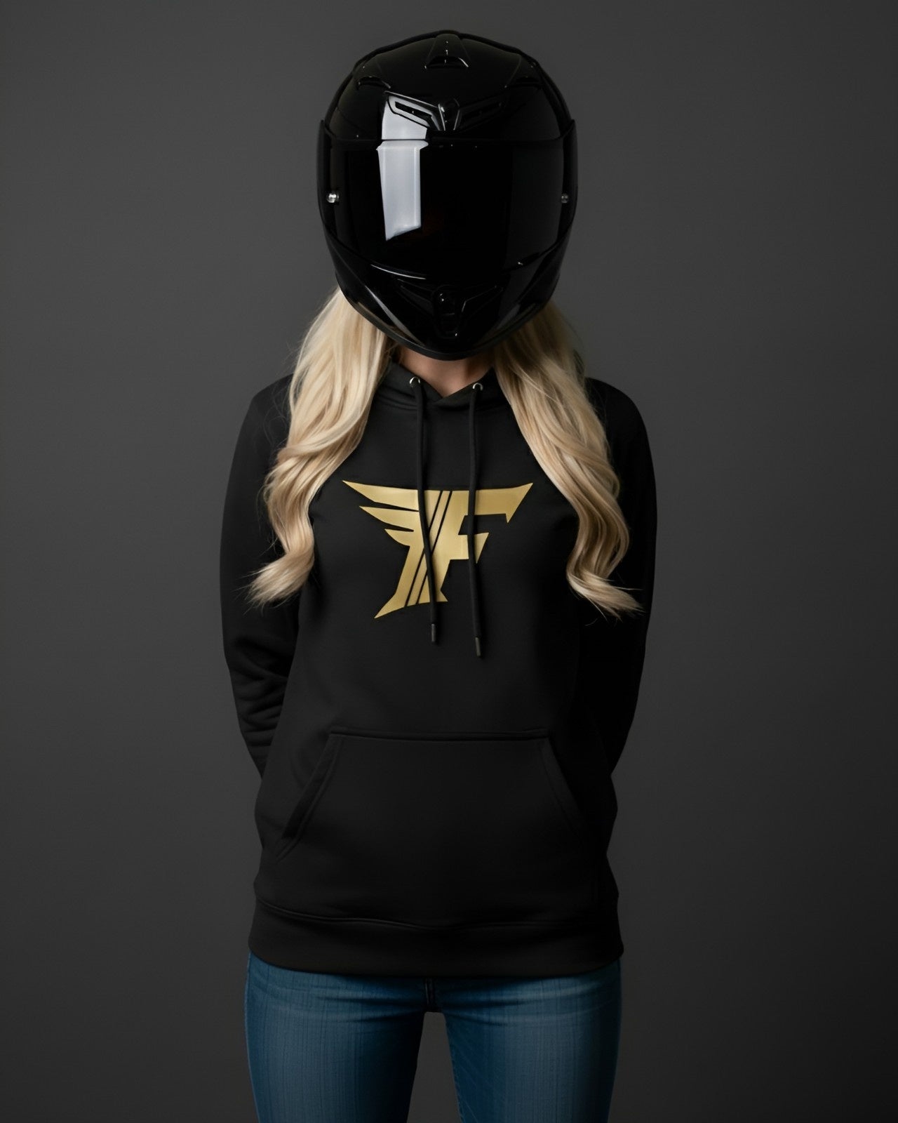 Black hoodie with gold winged "F" logo on the chest, modeled by a person wearing a shiny black motorcycle helmet and blonde hair over blue jeans.