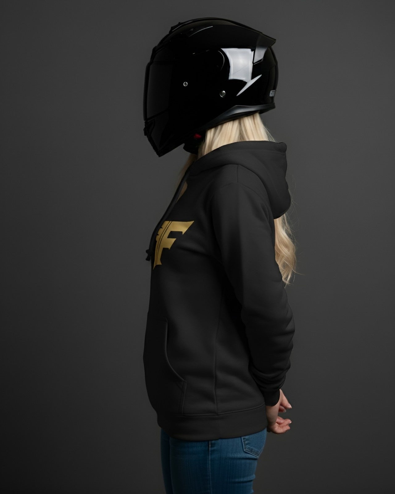 Person wearing a black hoodie with a gold logo and a black helmet on a dark background