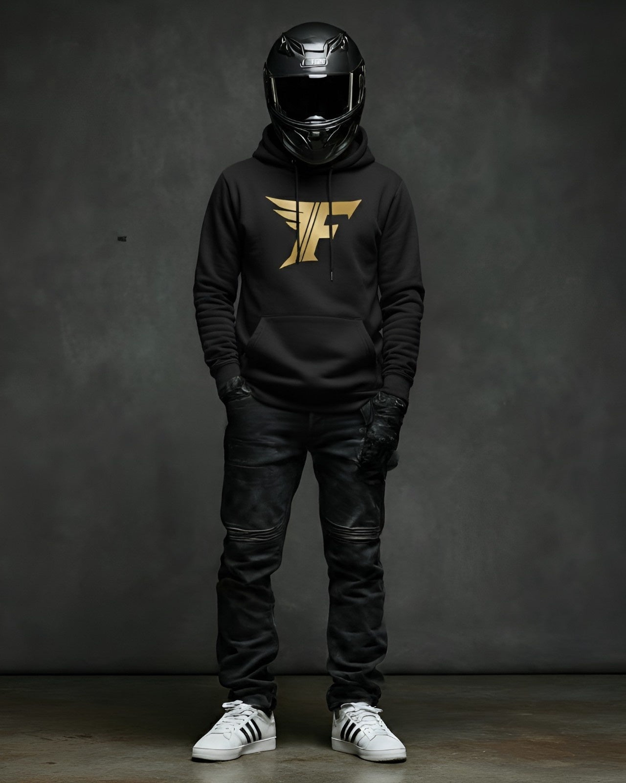 Man in full-face helmet wears black superbike t-shirt hoodie with gold winged "F" logo, black jeans, and sneakers. Motorcycle enthusiast apparel.