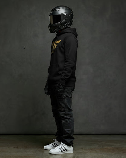 Person wearing a black helmet, black hoodie with a gold 'F' logo on the chest, black pants, and white sneakers against a dark background