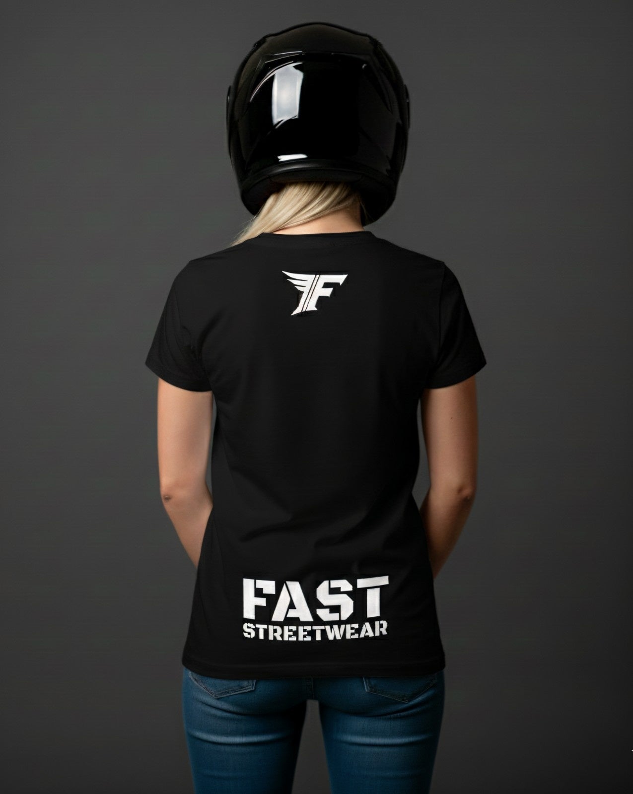 A woman wearing a black t-shirt, jeans, and a helmet, seen from the back. The shirt has a white 'F' wings logo on the neck and 'FAST STREETWEAR' near the bottom.