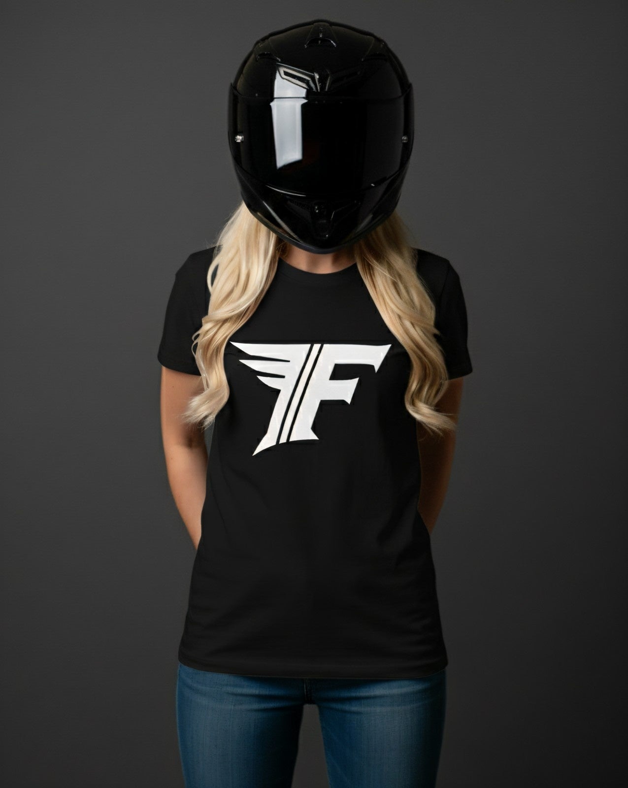 A blonde woman in a black motorcycle helmet, wearing a black t-shirt featuring a stylized white logo with an 'F' and wings.