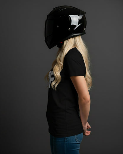A blonde woman in a black motorcycle helmet and a black t-shirt (product) with white text stands in profile against a gray backdrop.