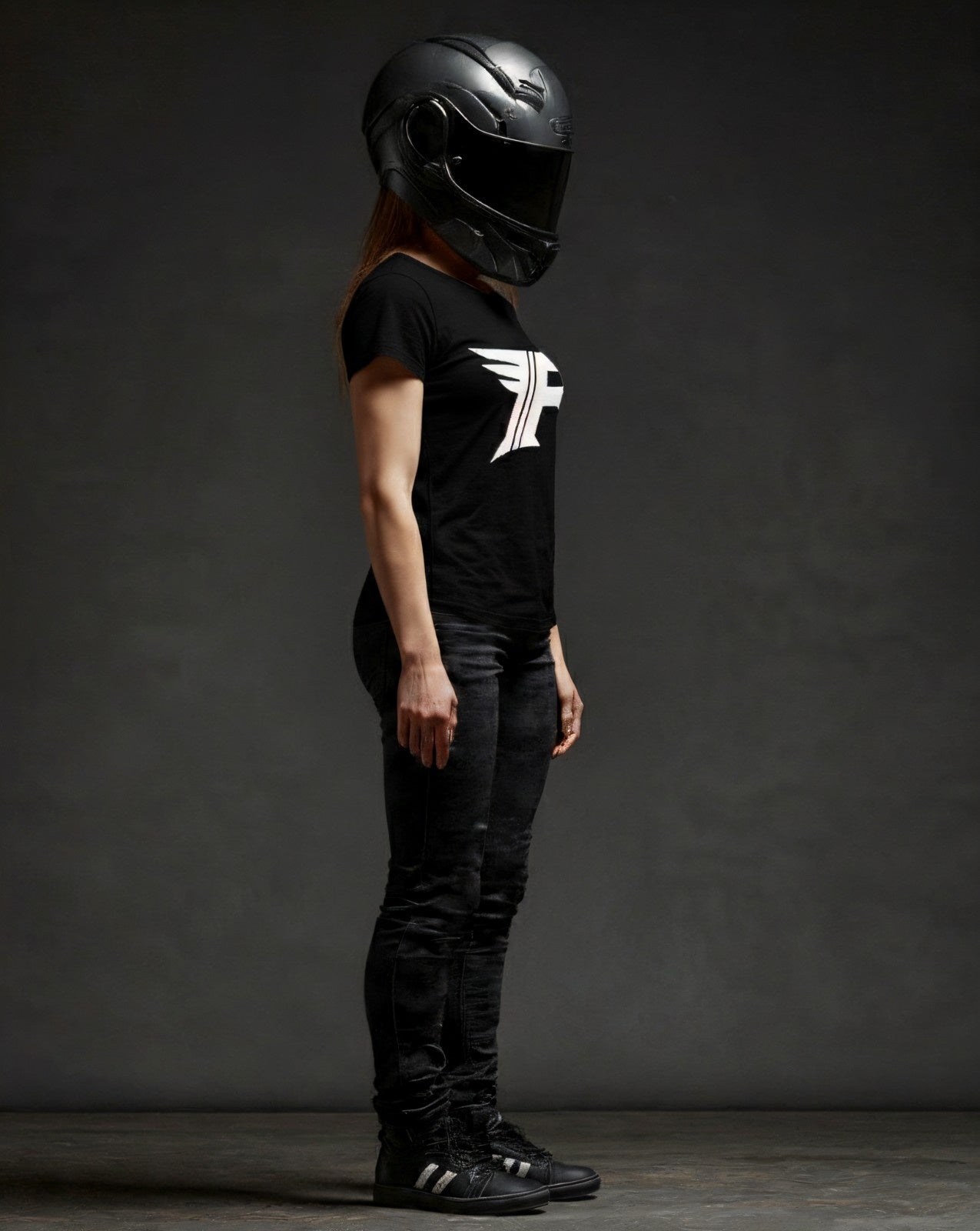 Person wearing a black helmet and black t-shirt with a logo against a dark background