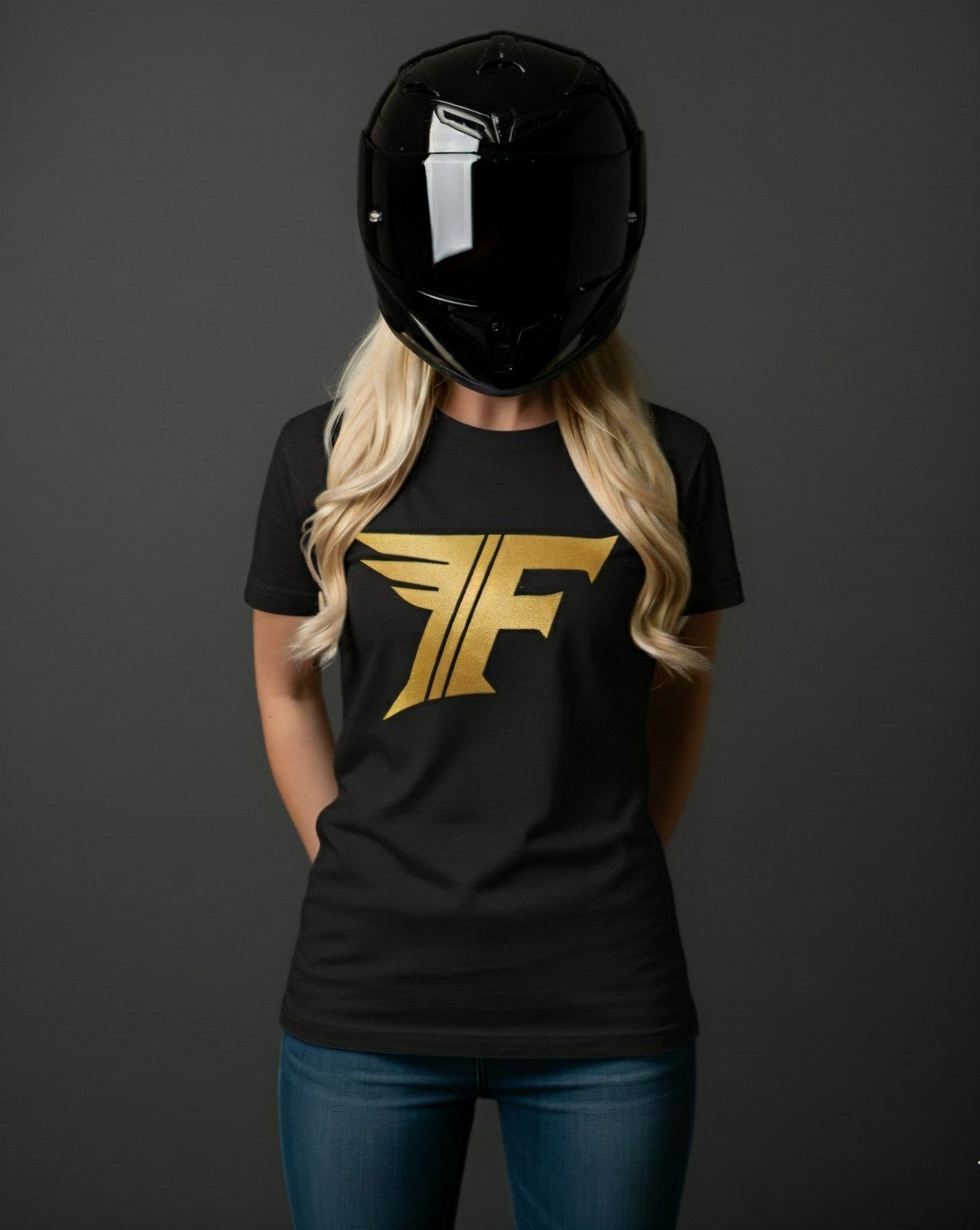 A blonde woman in a black helmet wears a black t-shirt with a metallic gold logo: a stylized 'F' with a wing extending from the top left.