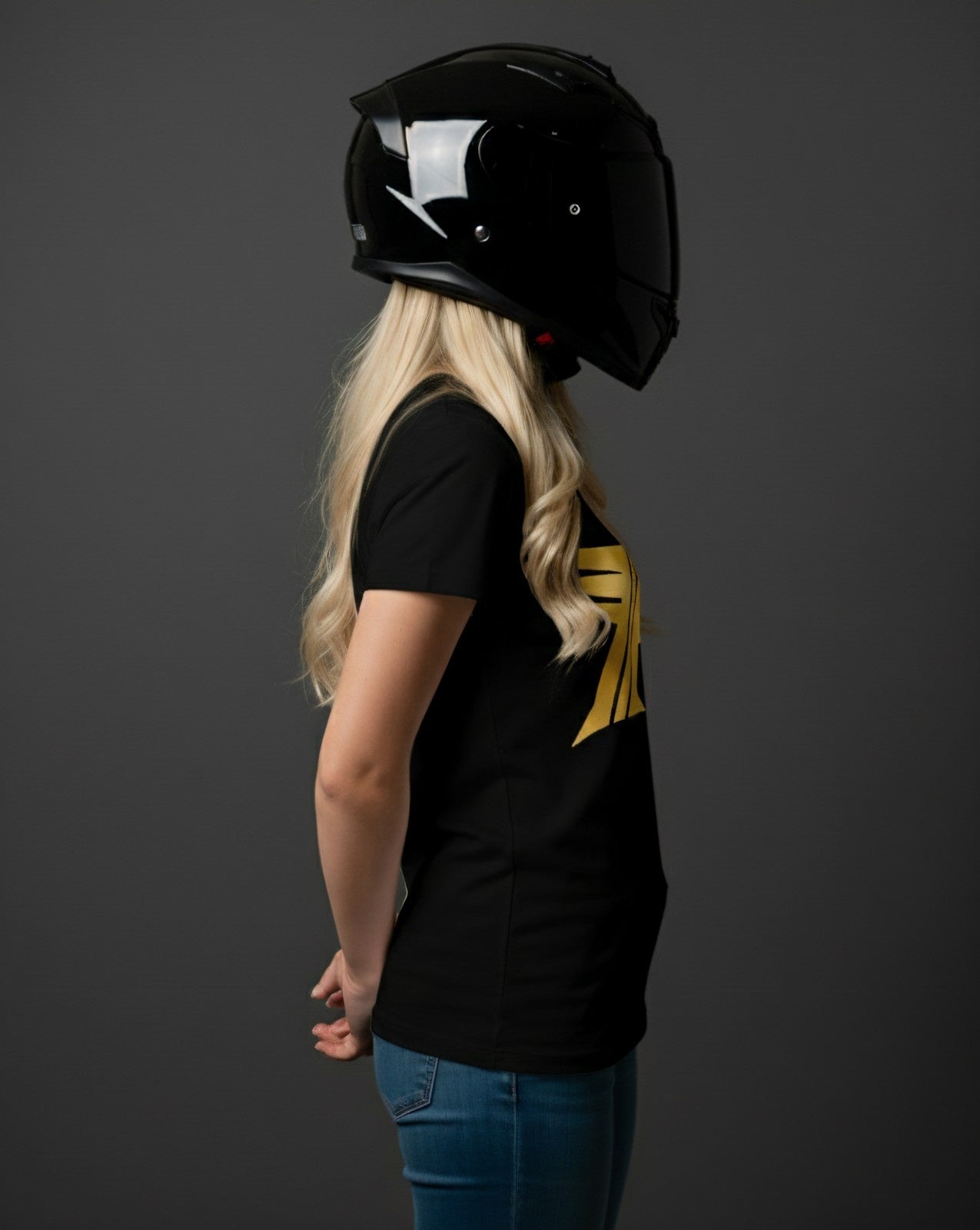 Person wearing a black helmet and black t-shirt with a gold logo on a dark background