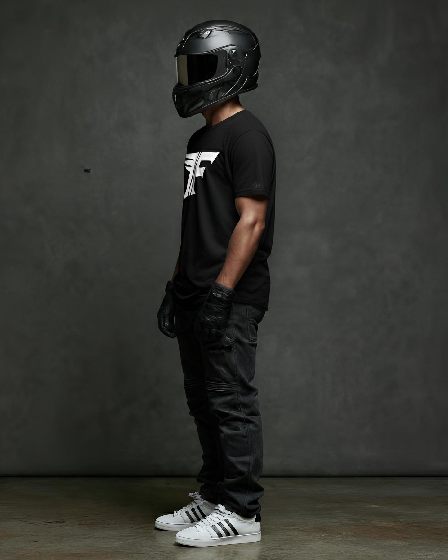 Person wearing a black helmet and black t-shirt with a logo, standing against a dark gray background.