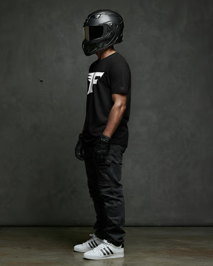 Person wearing a black helmet and black t-shirt with a logo, standing against a dark gray background.