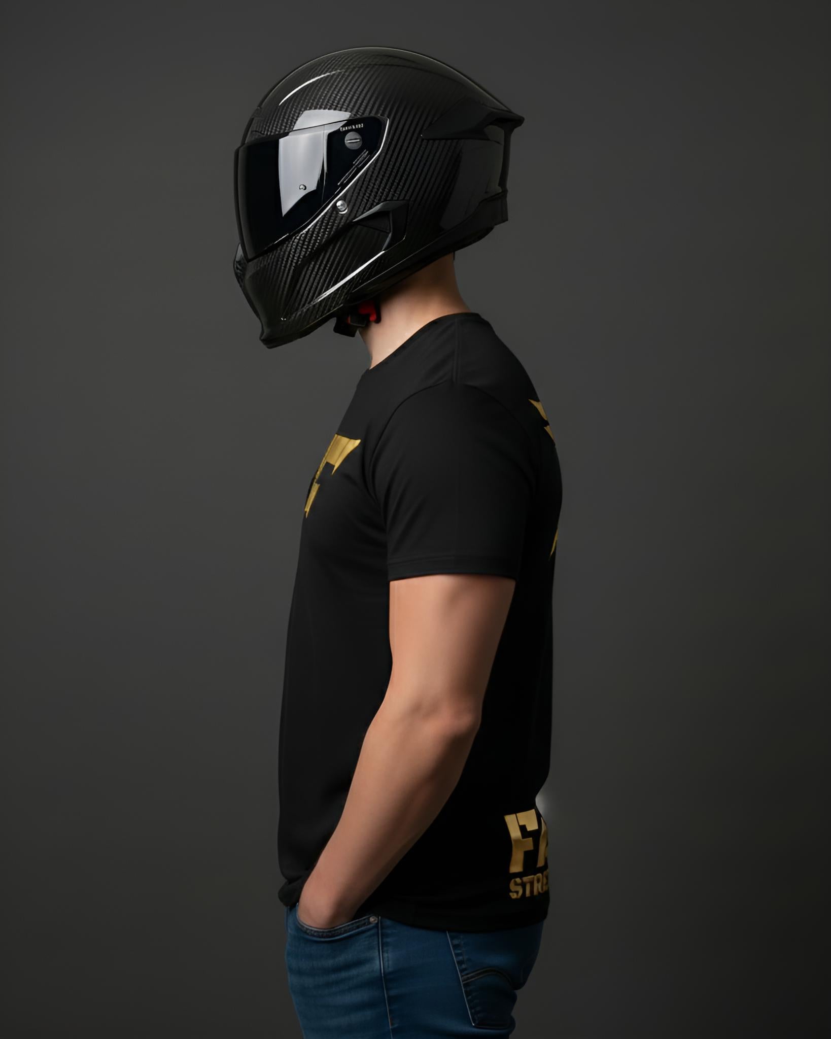 A person in profile wearing a carbon fiber motorcycle helmet and a black t-shirt with a gold graphic logo on the chest and lower torso.