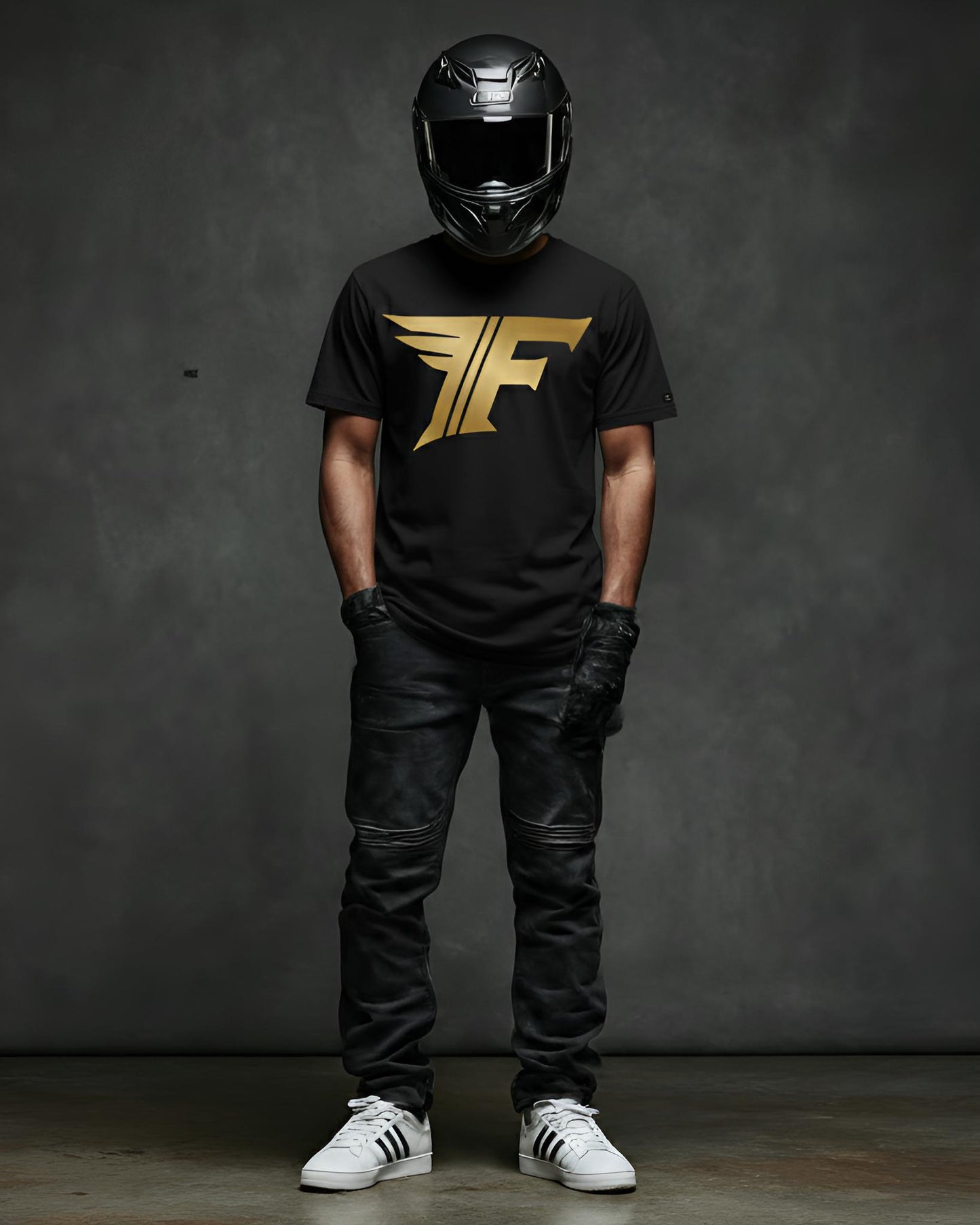 A man wearing a black shirt featuring a gold "F" logo with wings, black jeans, motorcycle gloves, a helmet, and white sneakers.