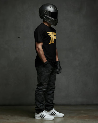 A person in a black shirt with a gold "F" logo, dark jeans, white sneakers, and a full-face motorcycle helmet, standing sideways.