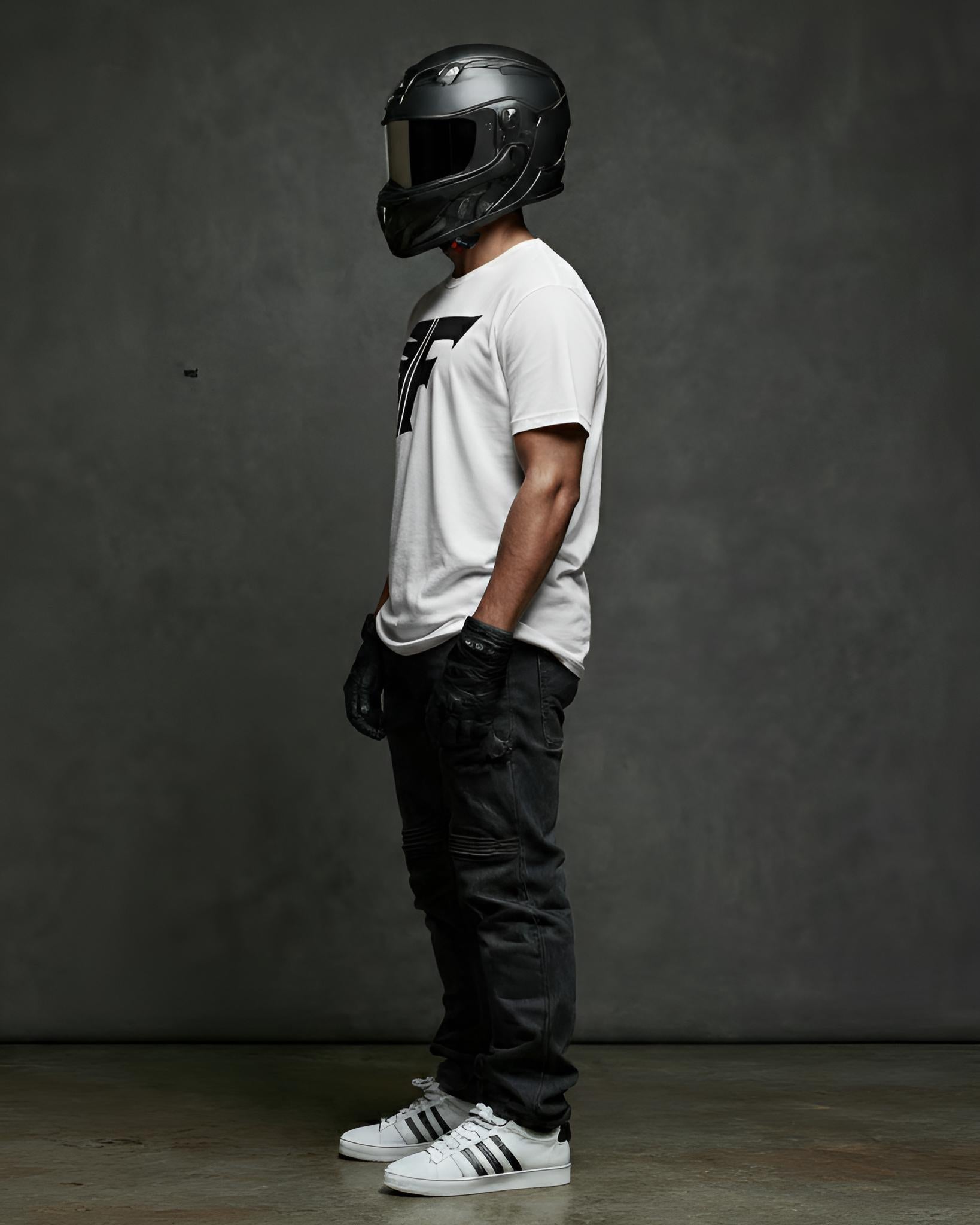 Person wearing a white t-shirt with a logo, black helmet, and black pants against a gray background