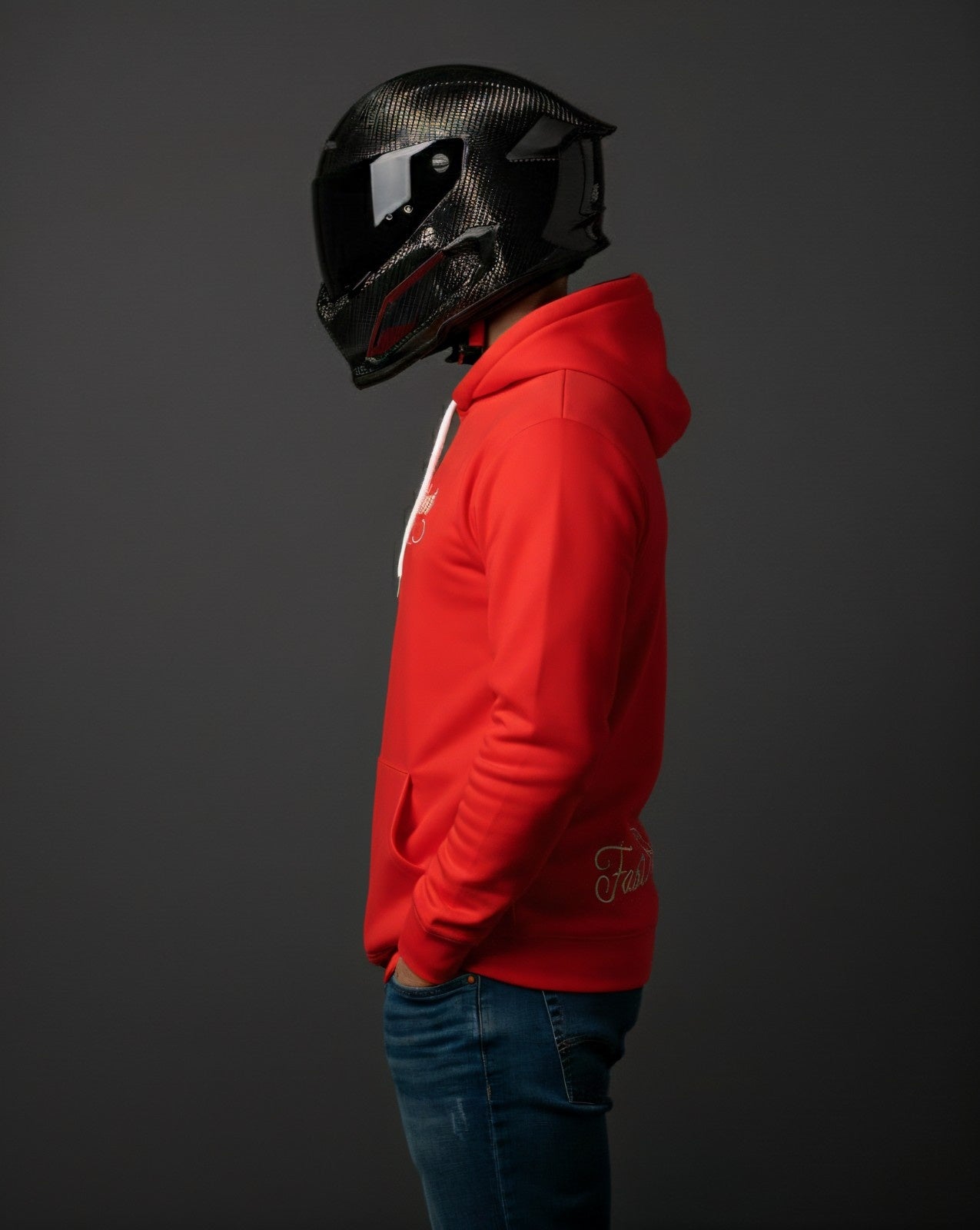 Person wearing a red hoodie and carbon fiber racing helmet on a dark background