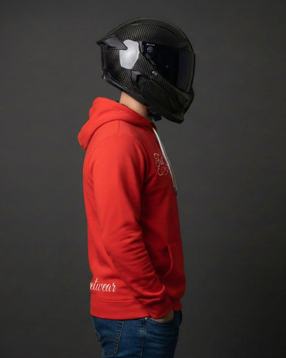 Person wearing a red hoodie with fast streetwear branding and a carbon black helmet on a dark background