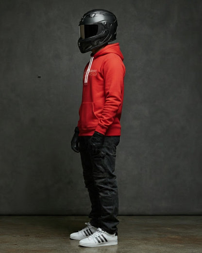 A man wearing a red Fast Streetwear cursive logo hoodie shirt with a Helmet (Racing), White Adidas superstars, and bkack jeans