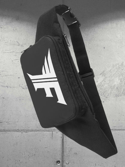 Black sling or fanny pack with a white winged 'F' logo, showing the adjustable strap and buckle. Presented against an industrial, gray wall.