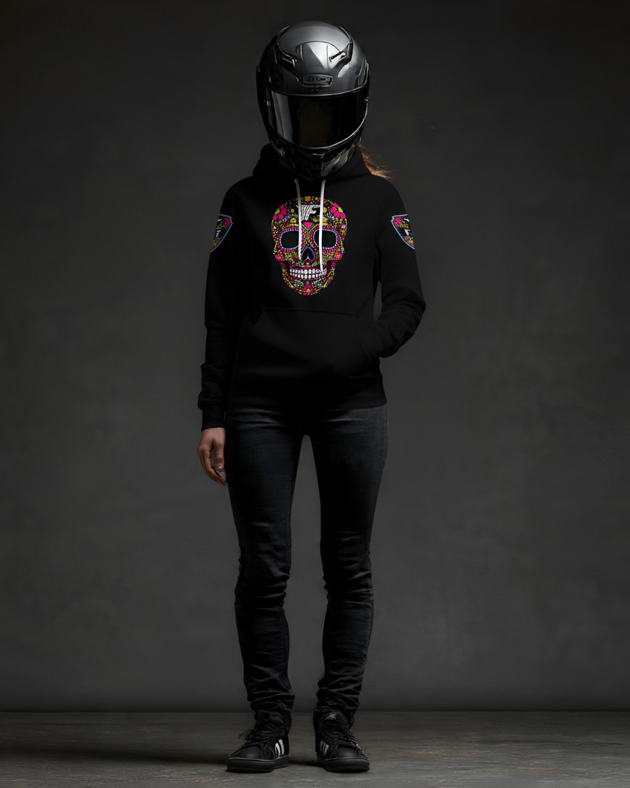 Black hoodie with colorful, detailed sugar skull design on the chest, worn by a figure in a motorcycle helmet and dark jeans. Patches on sleeves.