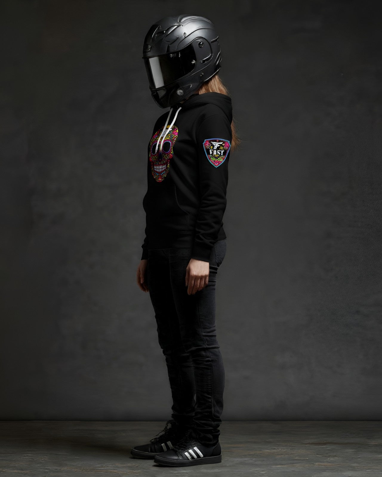 Left side profile of a black hoodie with a sugar skull design and a prominent sleeve patch, worn by a figure in a full-face motorcycle helmet.