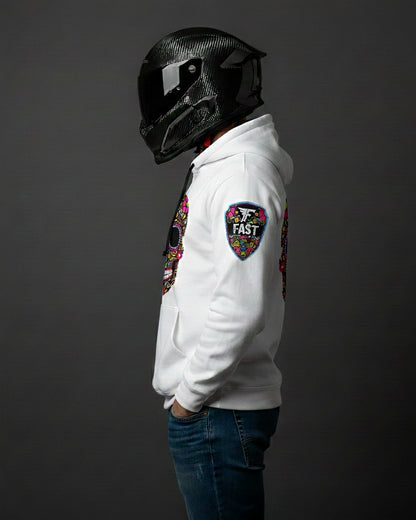 Left profile of the white sugar skull hoodie, showcasing the shield "FAST" logo patch on the left sleeve. Worn by a person in a motorcycle helmet.
