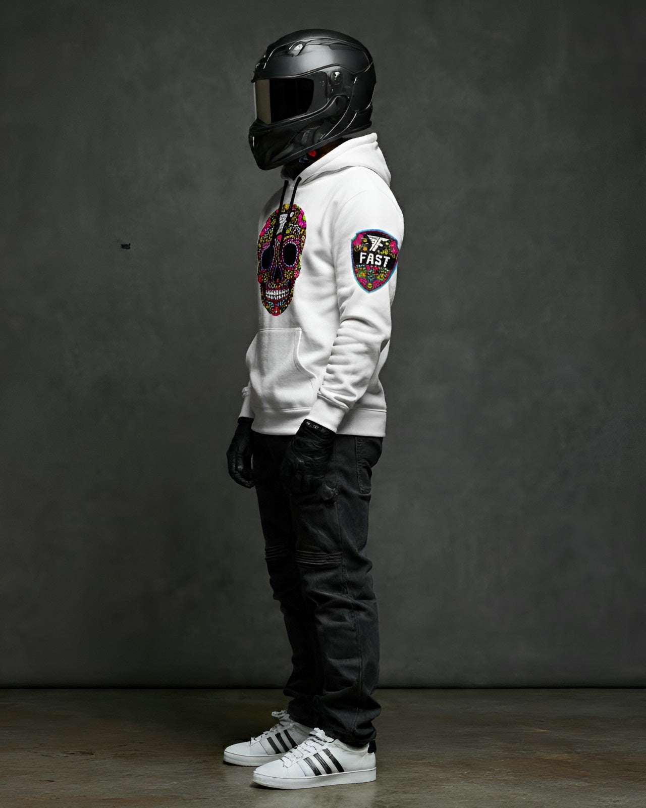 Left side view of the white sugar skull hoodie, showcasing the shield patch on the sleeve. Model wears a black helmet and jeans.