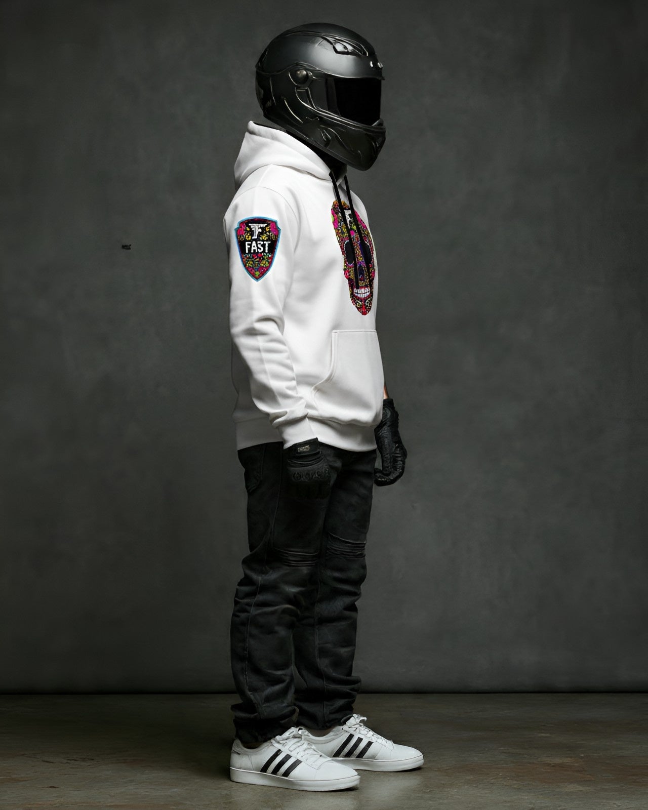 Right side profile of the white sugar skull hoodie, featuring the colorful sleeve patch detail. Model wearing a black helmet and gloves.